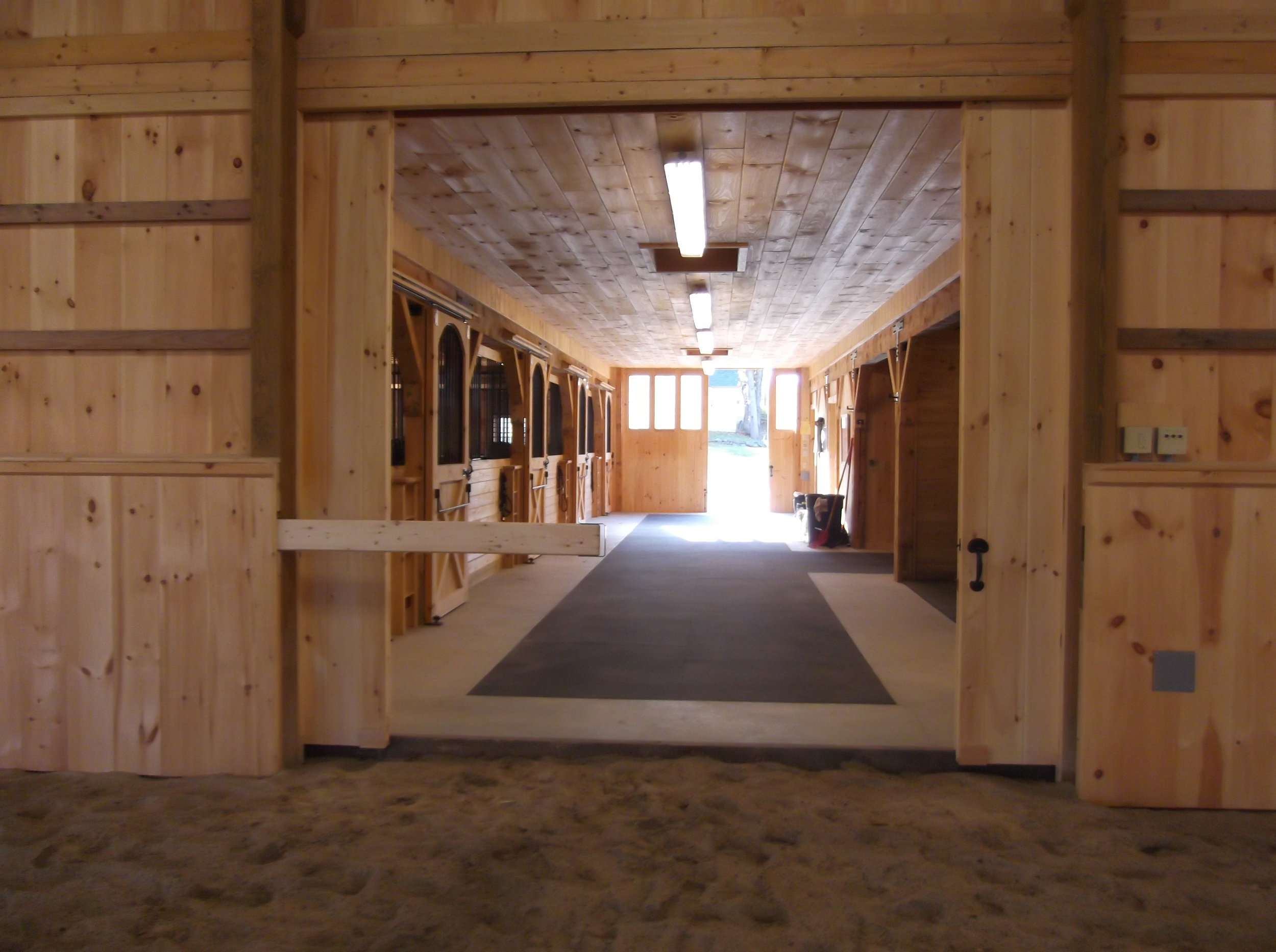  The image shows the inside of a large barn. The barn is made of wood and has a high ceiling. There are several horse stalls on either side of the barn, and there is a large open area in the center. The barn is well-lit and has a concrete floor. 