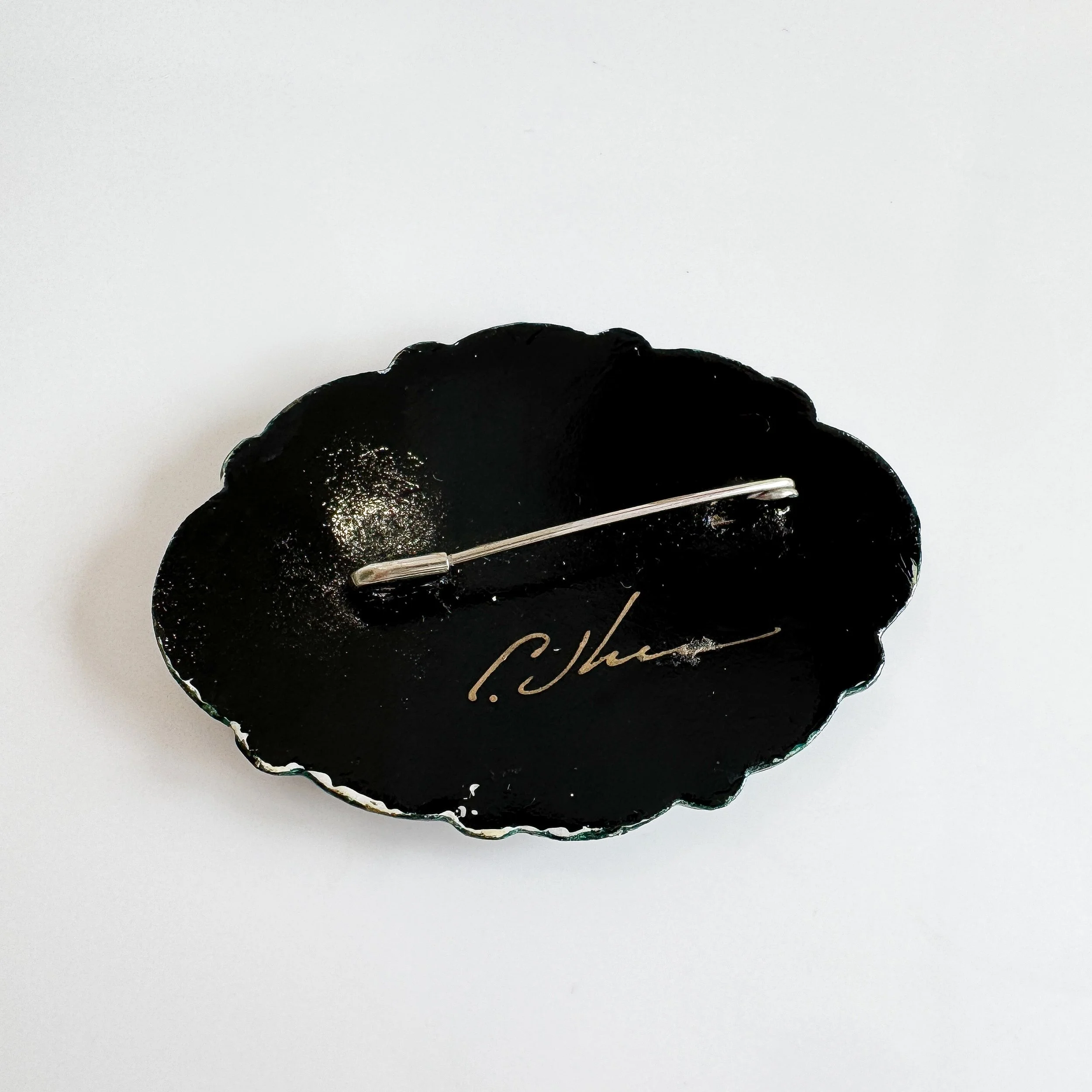 The back of the brooch which is all black with a pin fastening and a signature
