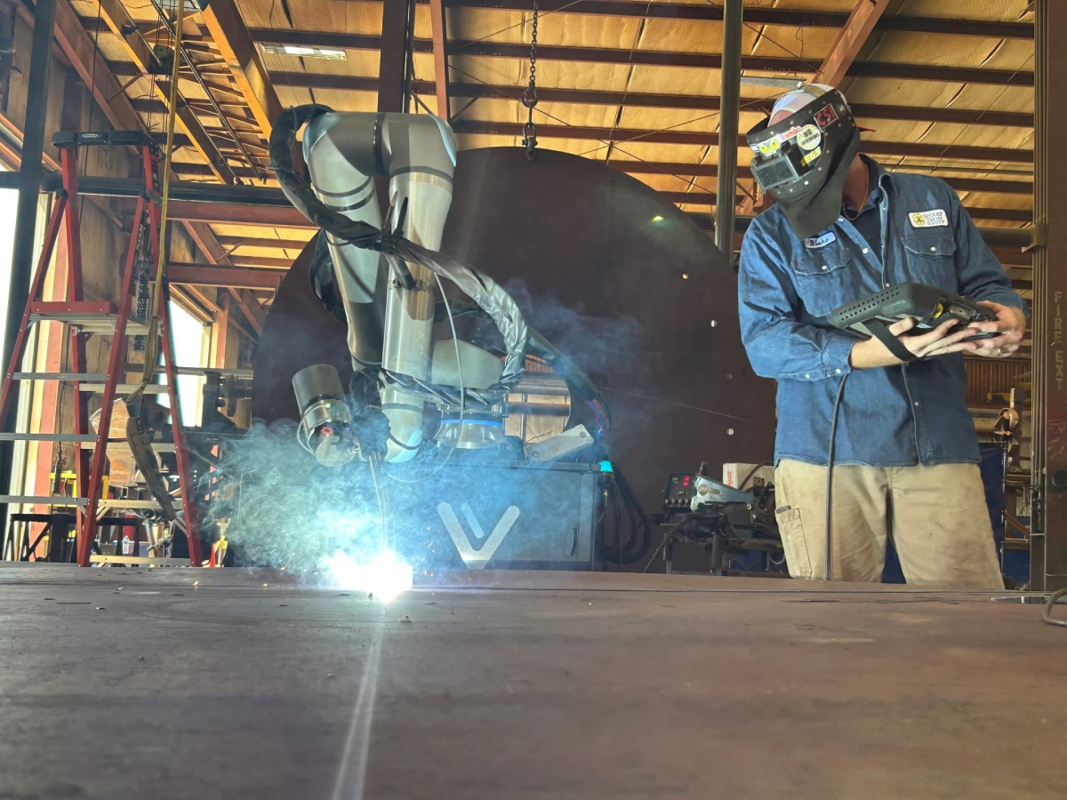Cobot welding system performing heavy-duty fabrication on large equipment components while an operator monitors the welding process in an equipment manufacturing shop environment.