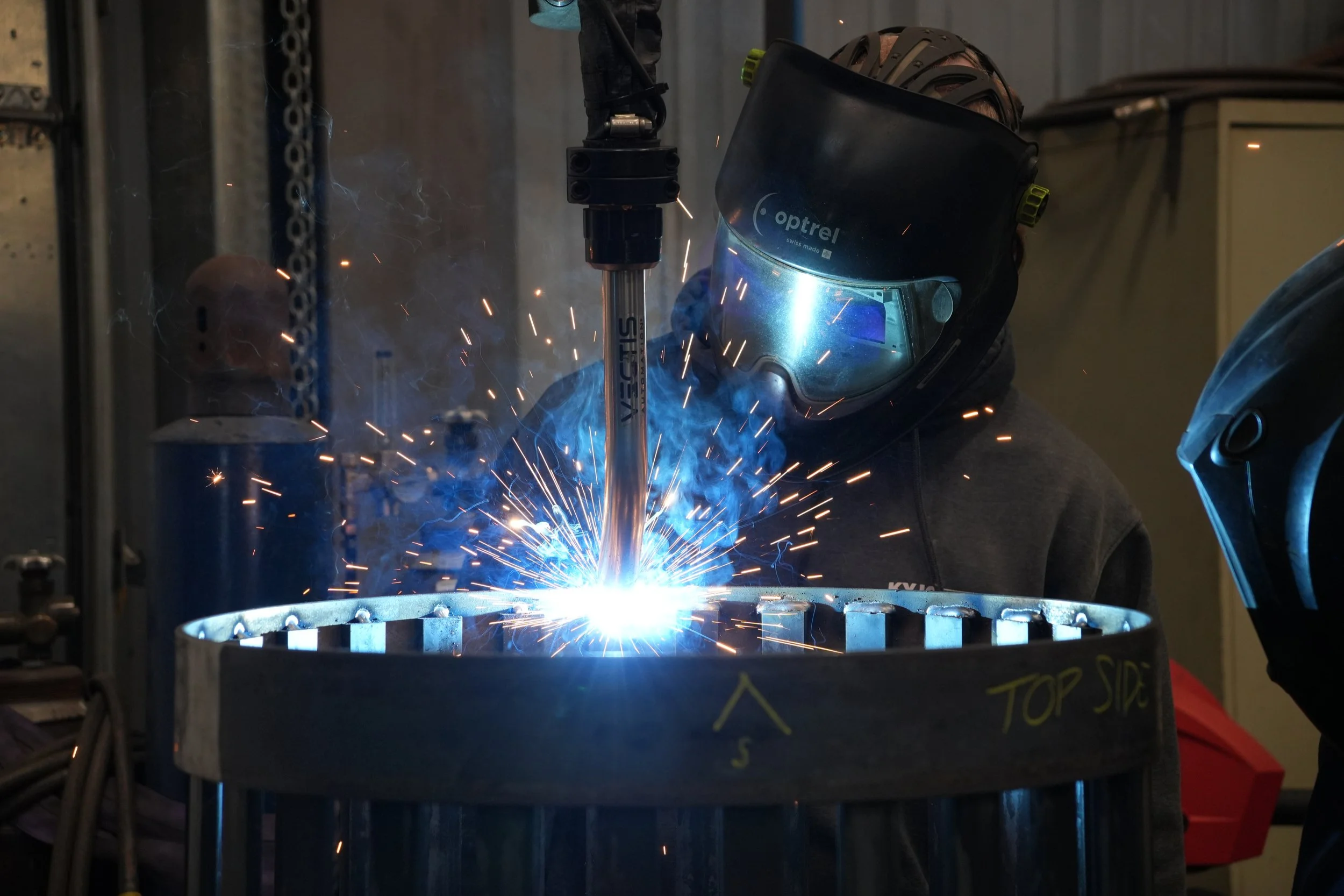 Operator monitors a Vectis cobot welding a circular steel assembly at KYJO Steel.