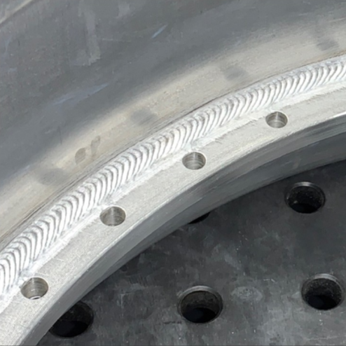 Circumferential aluminum weld on a wheel assembly, showing a uniform bead profile