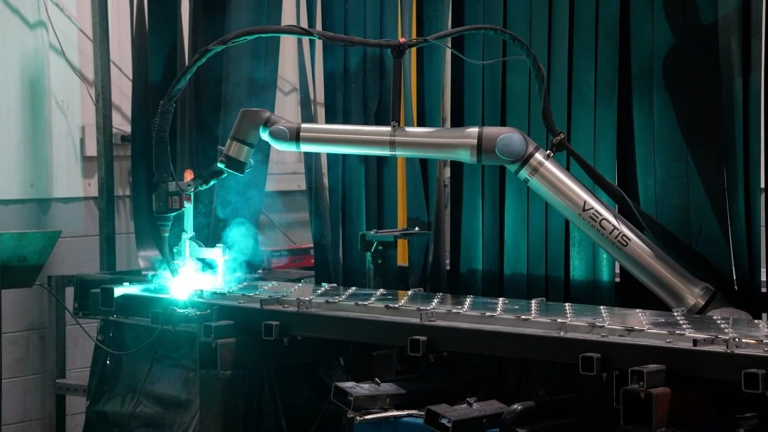 Vectis cobot welding system performing an automated weld along a large metal fabrication assembly table.