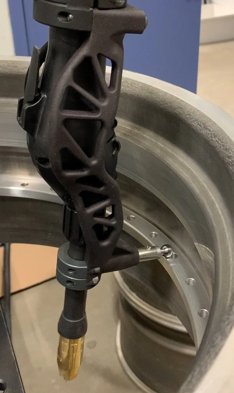 Cobot welding torch mounted on a robotic arm welding an aluminum rim, showing precise positioning near bolt holes and flange edge in an automated aluminum manufacturing process.