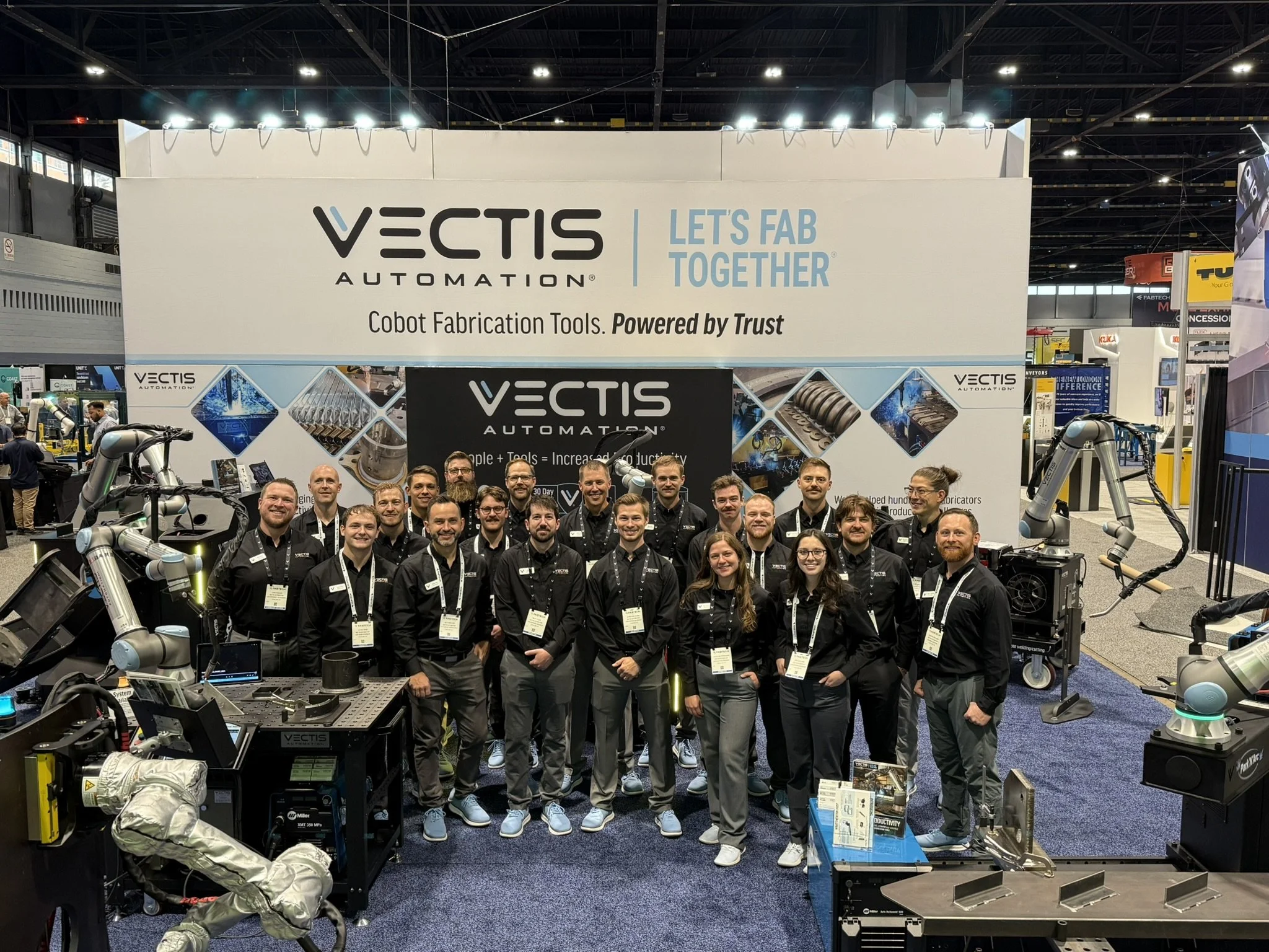 Vectis Automation team standing at the FABTECH booth with cobot welding and plasma cutting systems on display.