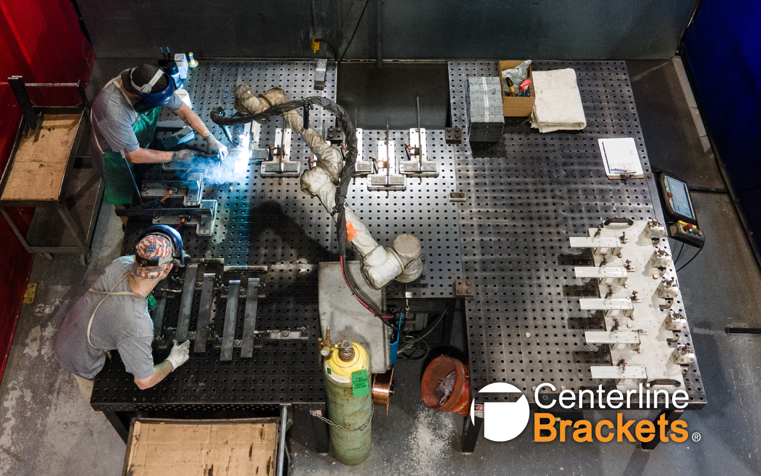 Overhead view of a Vectis cobot welding workcell at Centerline Brackets with operators working around a fixture table.