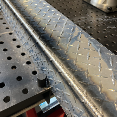 Close-up of a welded outside corner on a fabricated aluminum box, showing a uniform weld bead and consistent weld appearance along the edge.