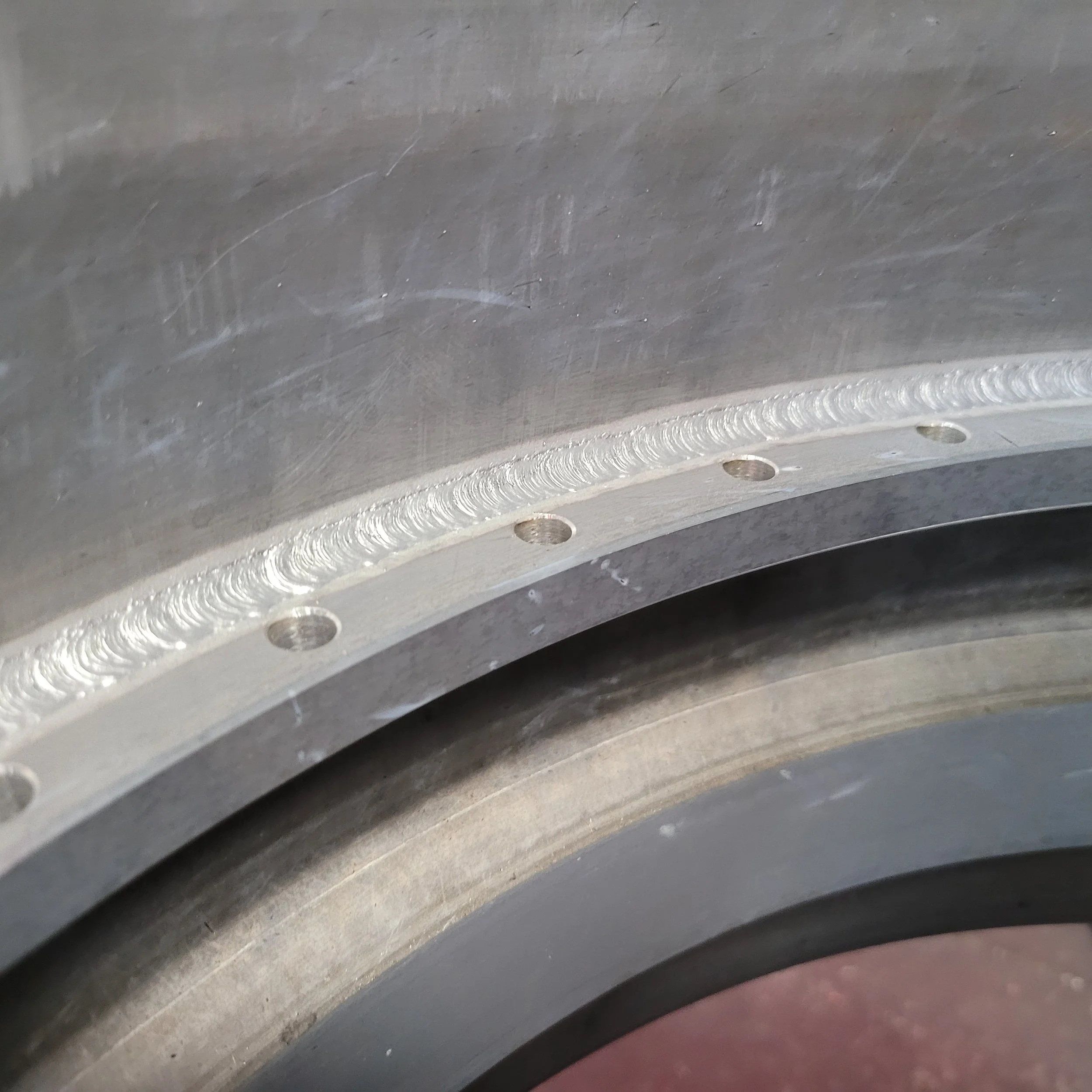 Close-up of a welded aluminum rim flange with evenly spaced bolt holes, showing weld bead consistency, smooth surface finish, and precision from an automated cobot welding process in aluminum manufacturing.