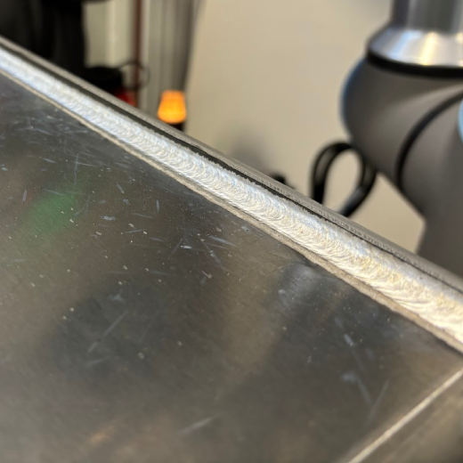 Outside-corner weld on a fabricated aluminum hydraulic tank, showing a consistent weld bead and uniform weld appearance along the tank edge.