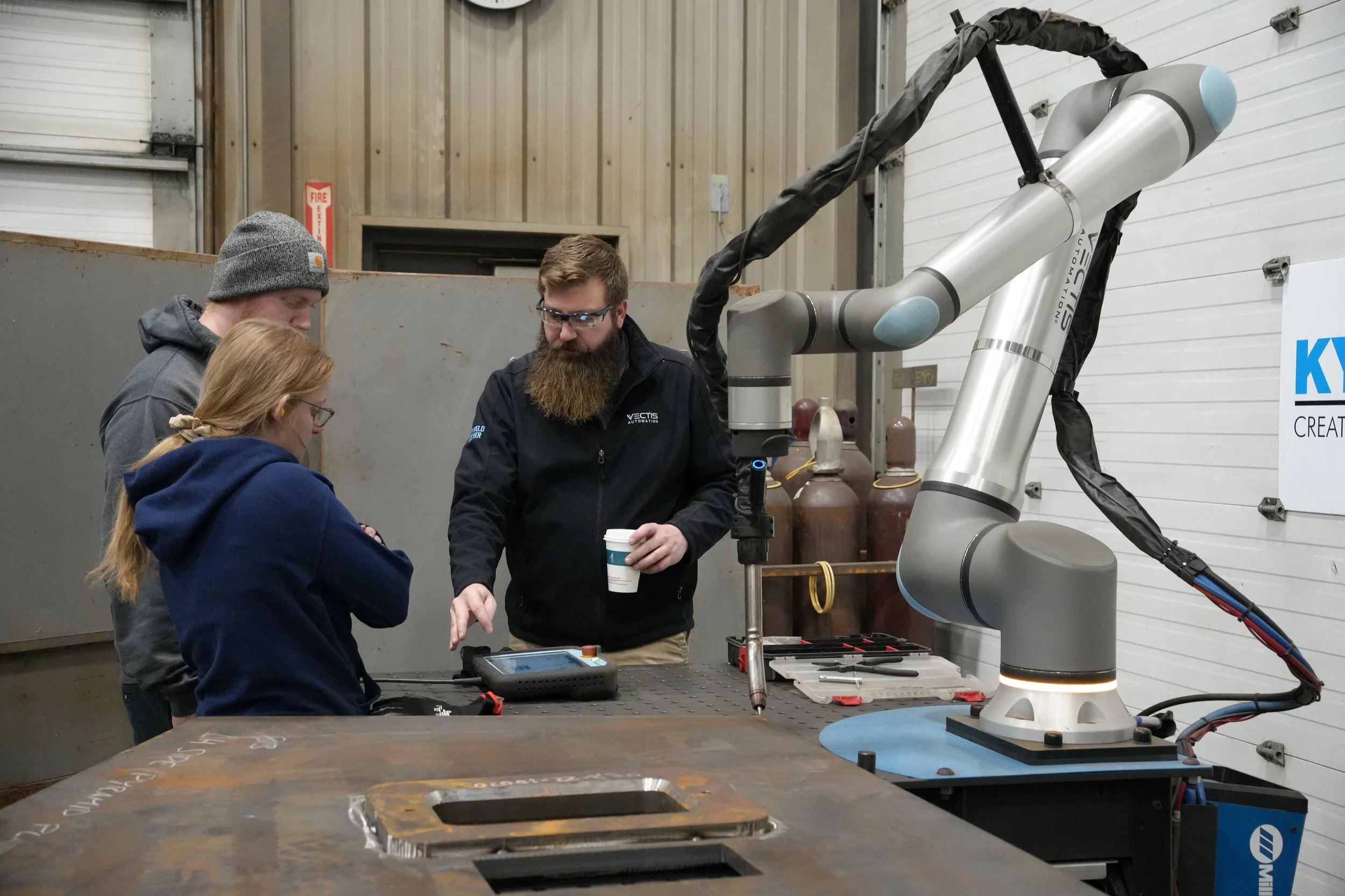 Vectis representative reviews cobot welding controls with KYJO Steel operators beside the welding system.