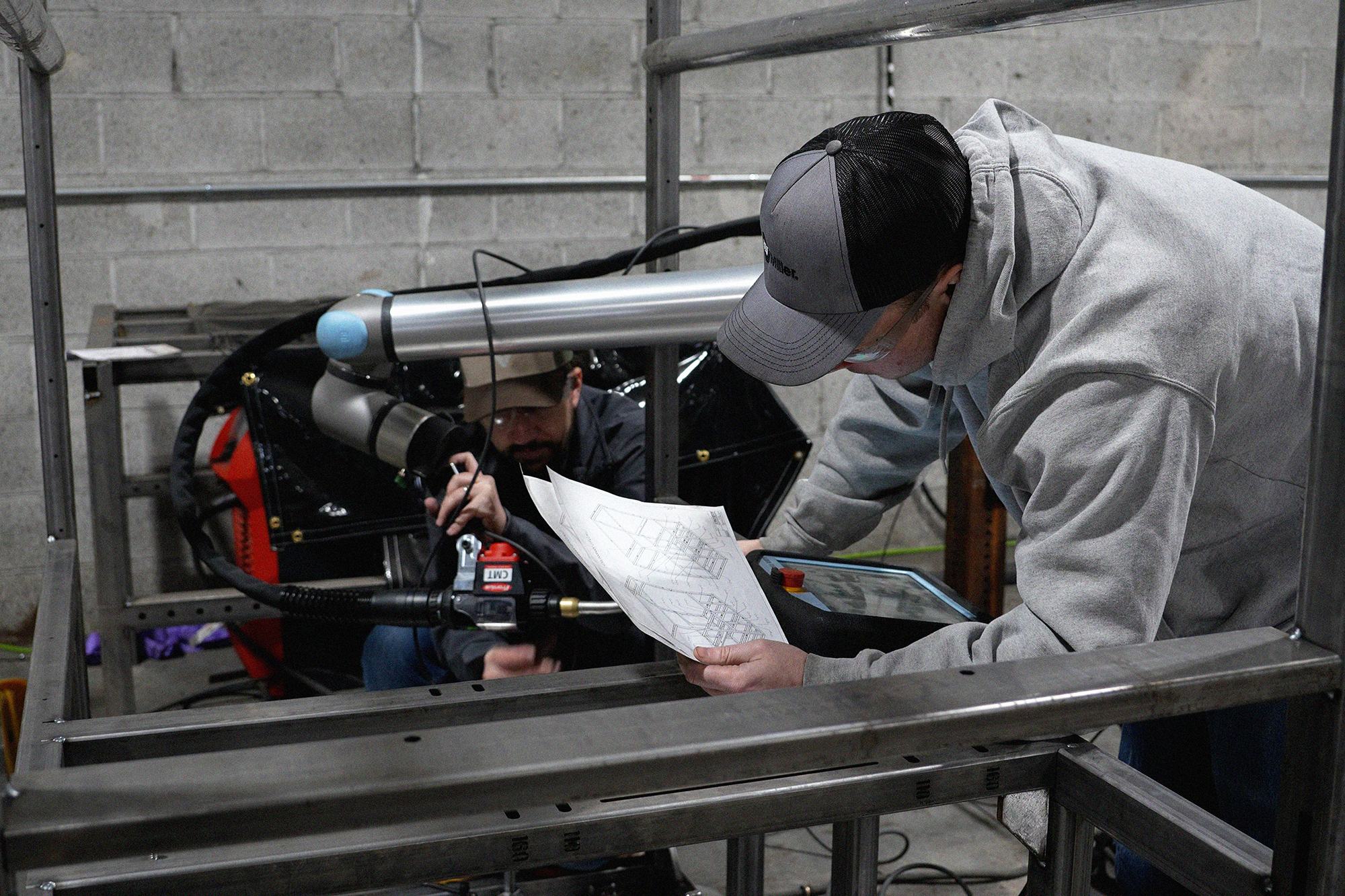 Two Caltech Manufacturing team members review a drawing and set up a Vectis cobot welding system for a large metal frame.