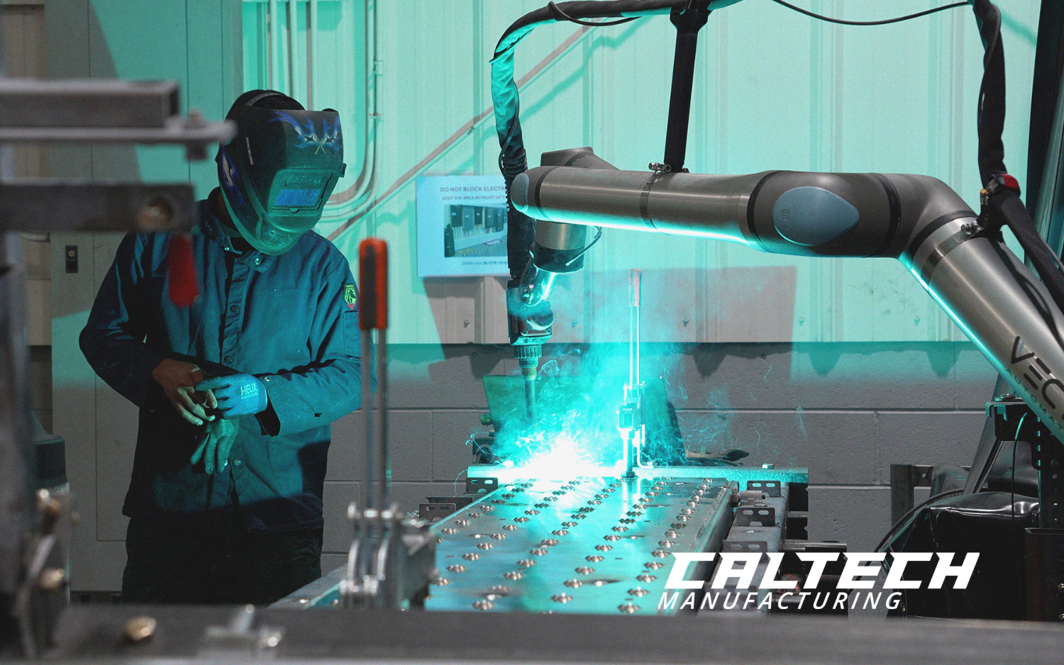 Vectis cobot welding system performing a weld while an operator monitors the process at Caltech Manufacturing.
