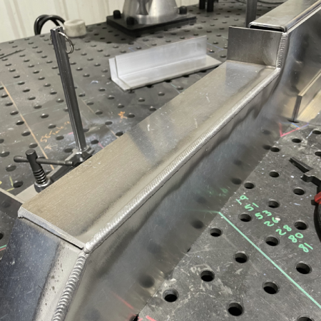 Long outside-corner weld on a fabricated aluminum box assembly, showing a consistent bead profile and clean weld appearance.