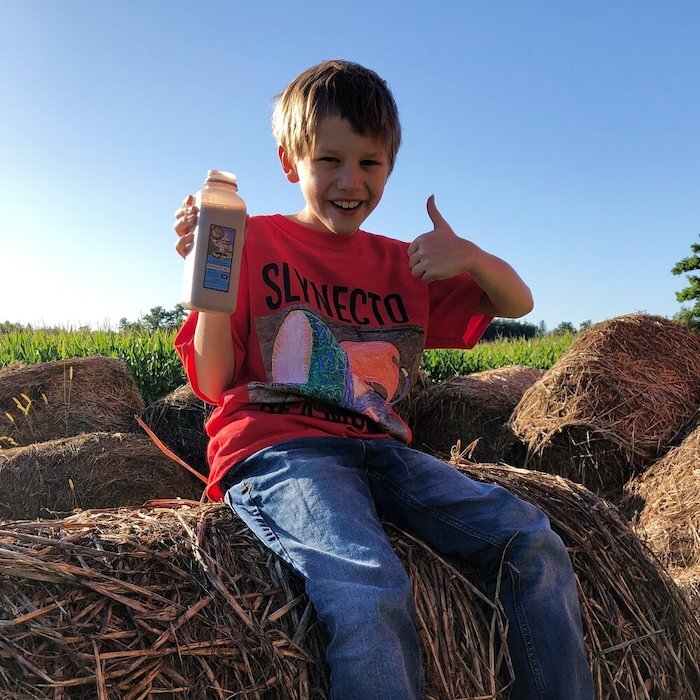 Young boy sitting on bale of hay gives High Lawn chocolate milk thumb’s up.
