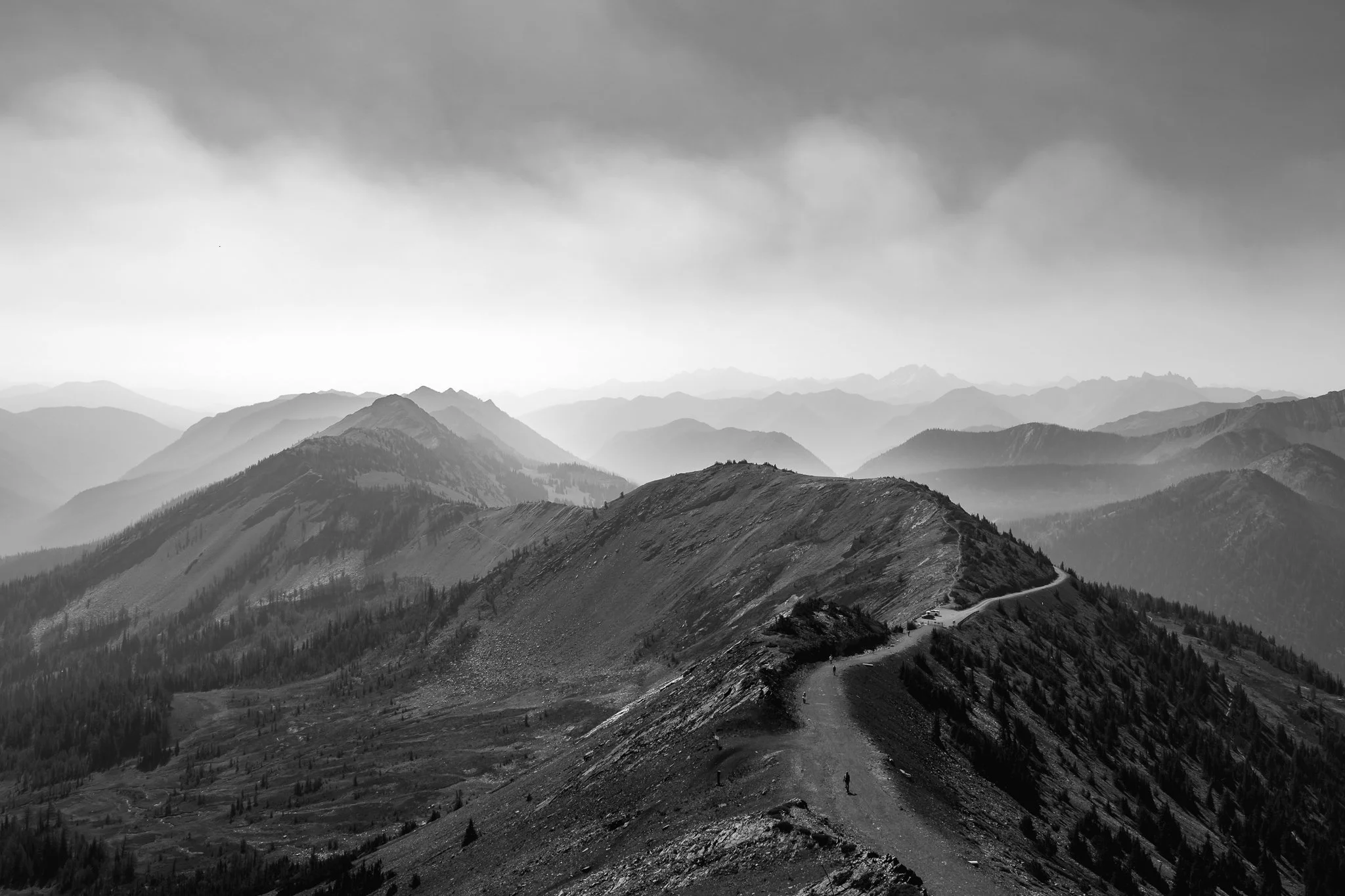 Looking down from Slate Peak at a high-altitude ridge road, where the distant mountains disappear into a glowing, monochromatic haze.