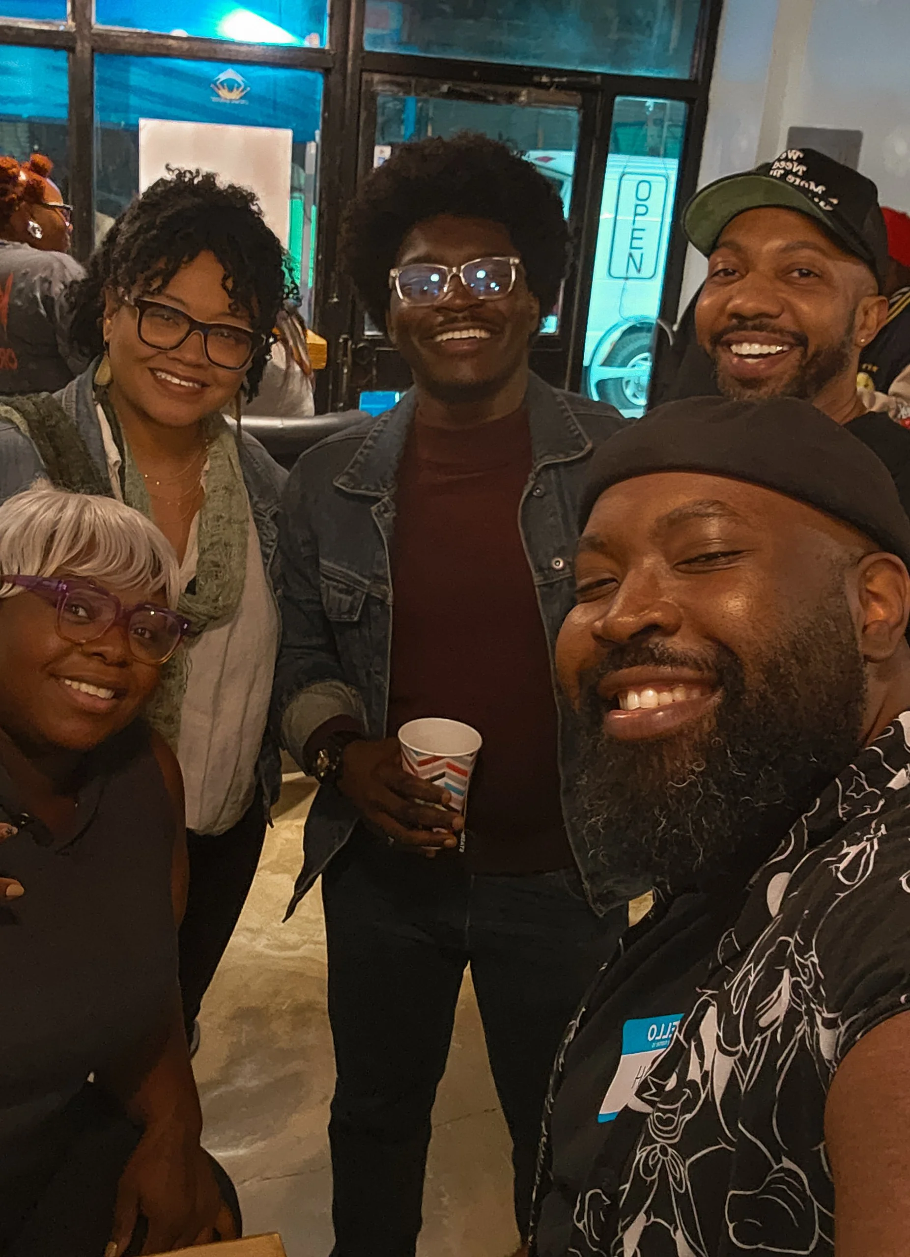 A group of diverse smiling people taking a selfie together indoors.