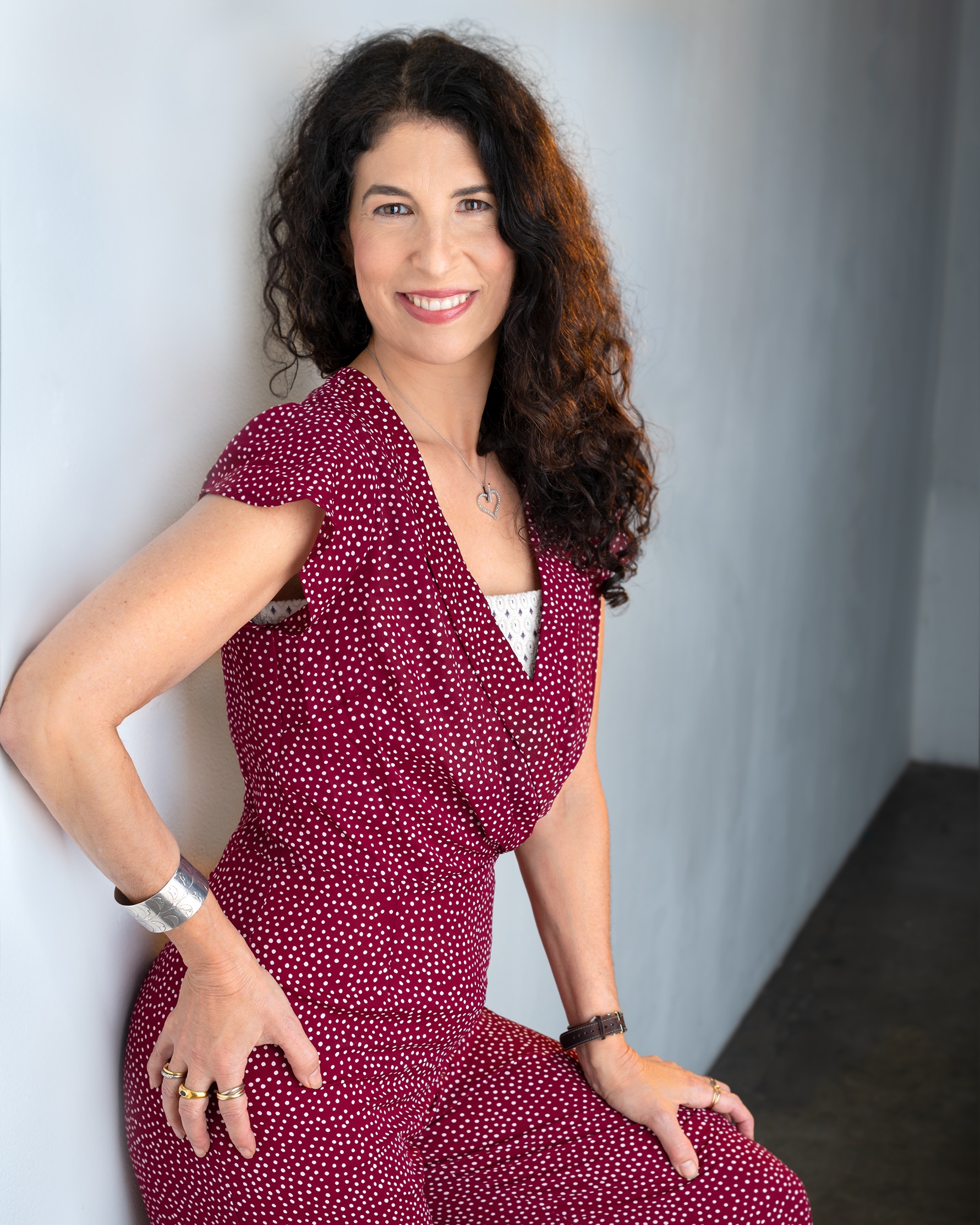 Denise Weisner, author and fertility expert, leaning up against a wall wearing a red jumper