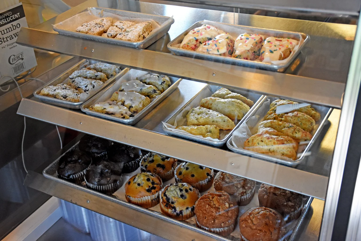 Assorted baked goods including various muffins and scones displayed in a glass-front bakery display case.