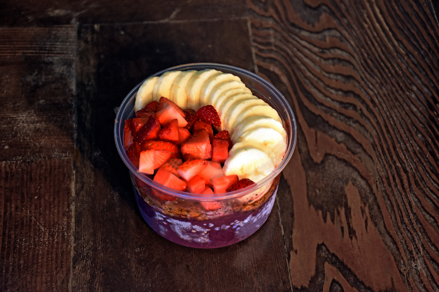 Açaí bowl filled with sliced bananas and strawberries on a wooden table.
