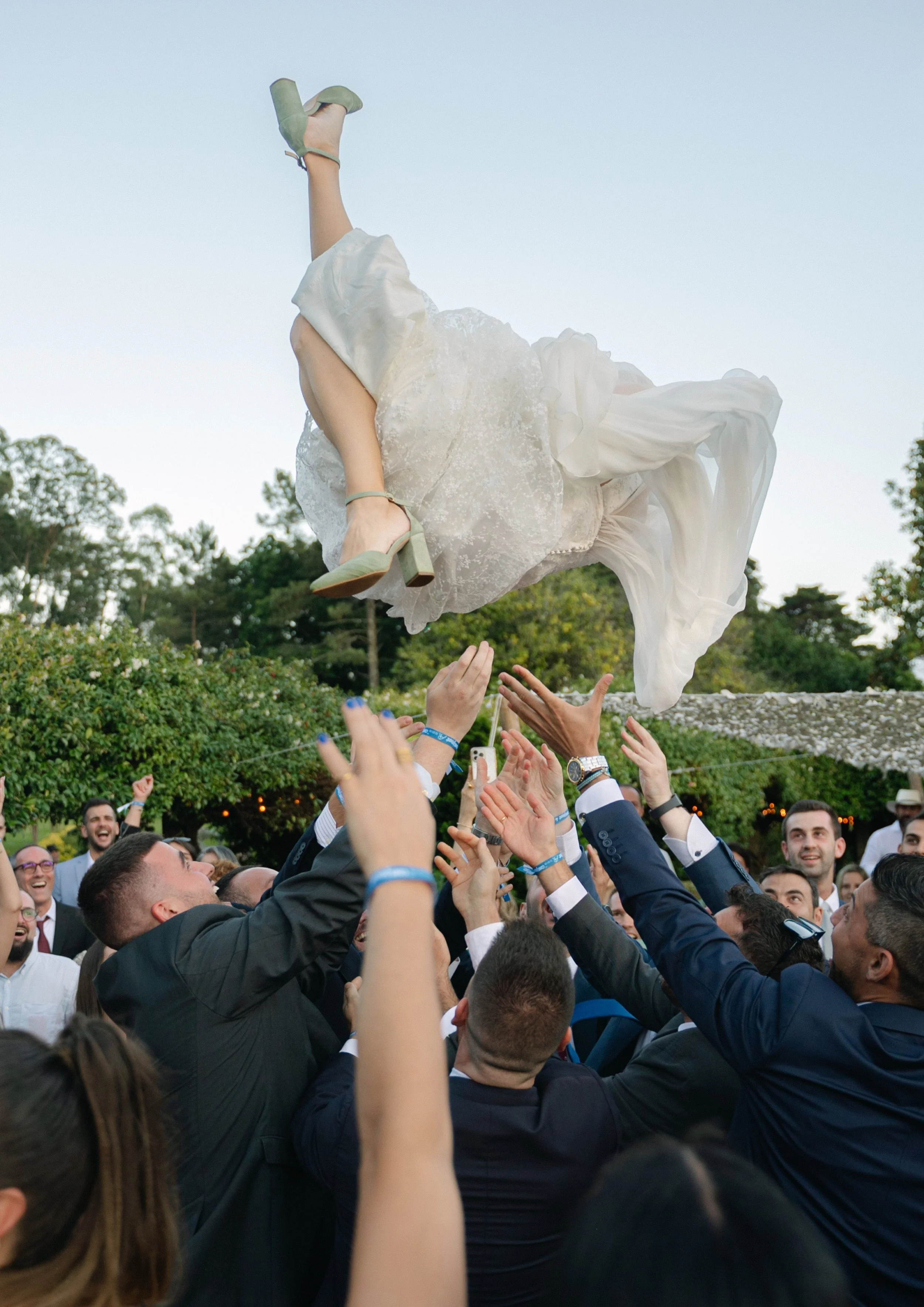 Grupo de personas en una celebración lanzando a una mujer con vestido de boda al aire mientras ella cae en medio de la multitud.