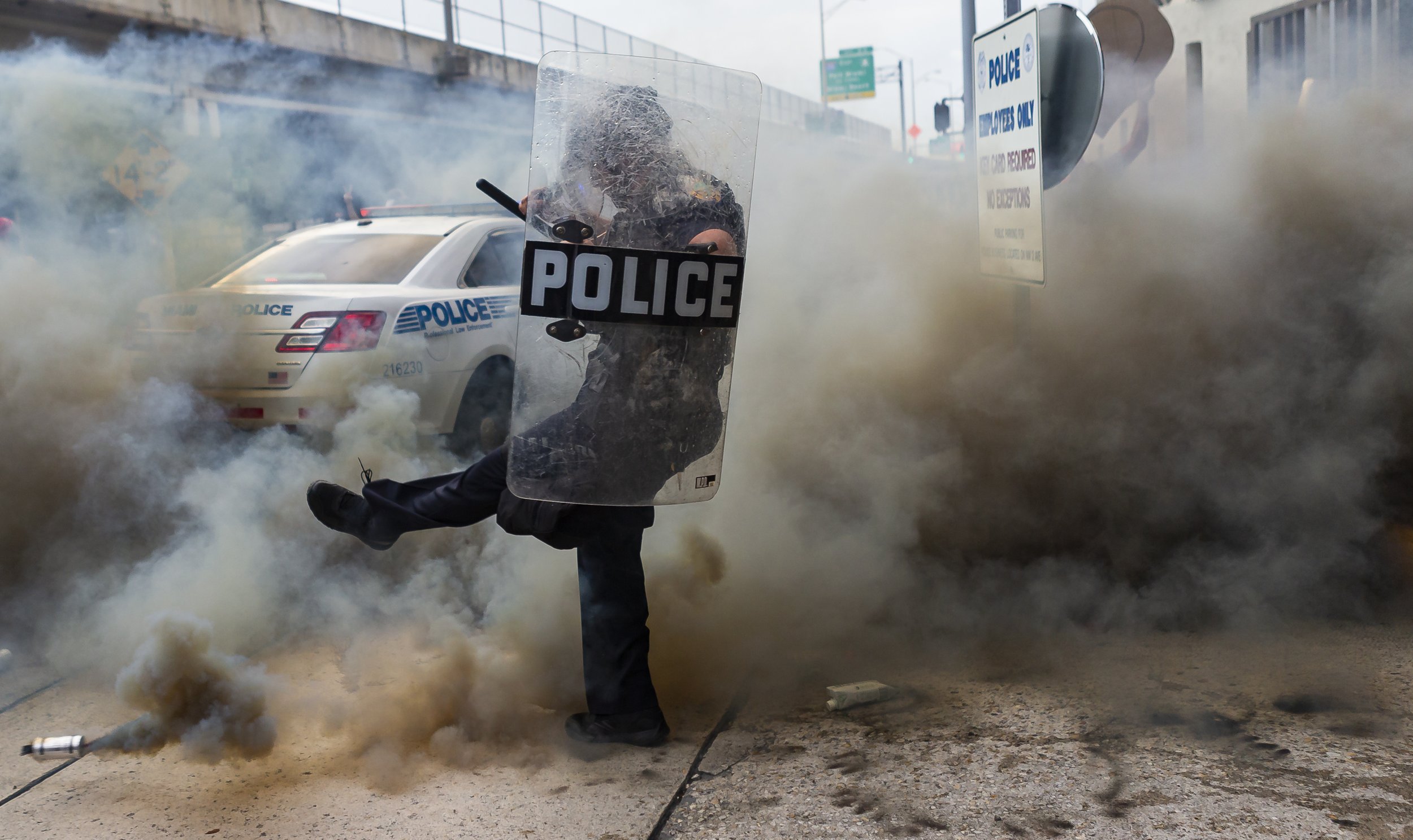  A police officer kicks a can spewing smoke during a “Justice for George Floyd” protest in downtown Miami on Saturday, May 30, 2020.  