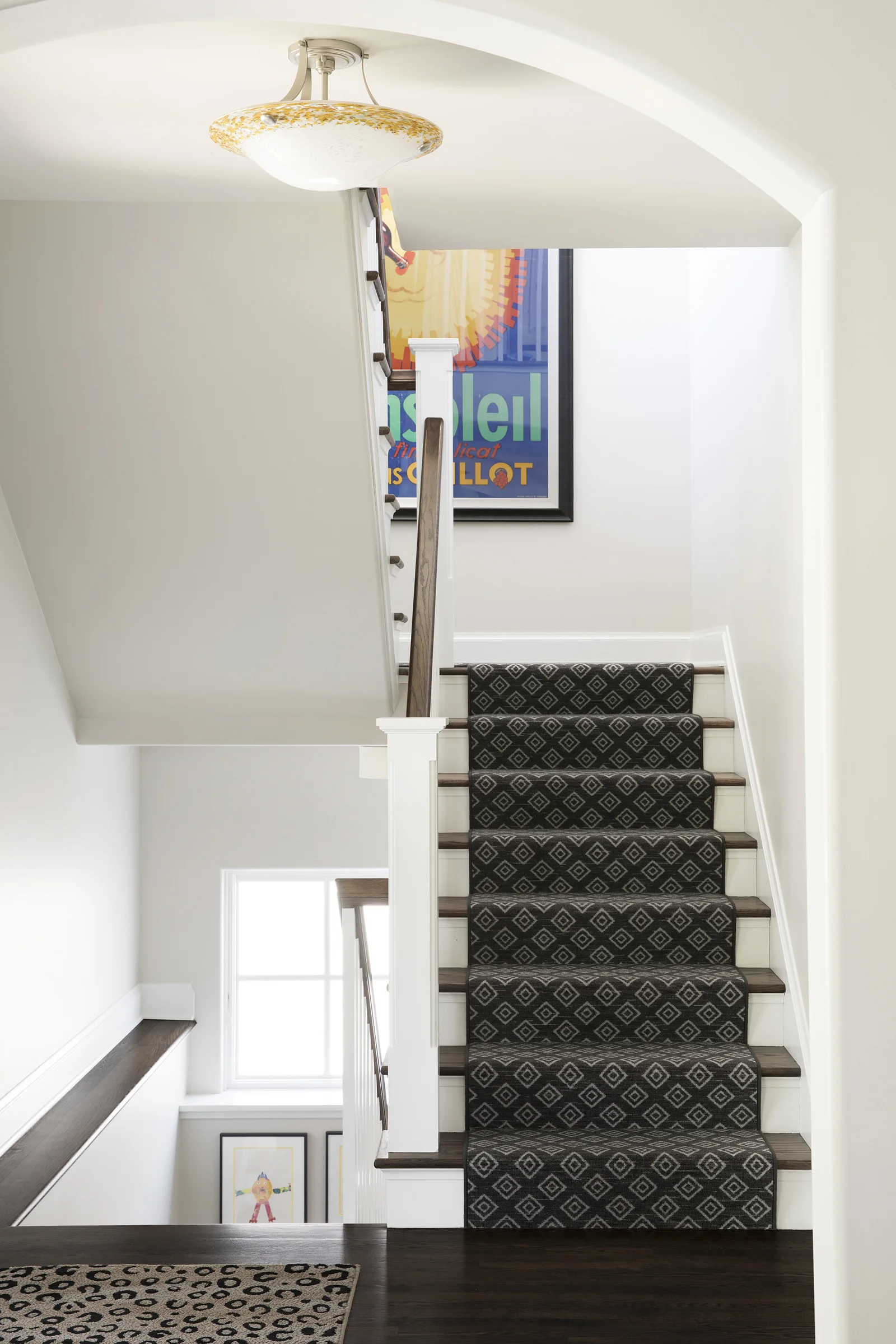 After: The large artwork on the landing came from the client’s previous home and set the direction of the color palette. We added carpet wherever possible for sound absorption and soft landings. I love the kid art that we hung on the lower landing, and how the existing entry light feels like we chose it for this space!
