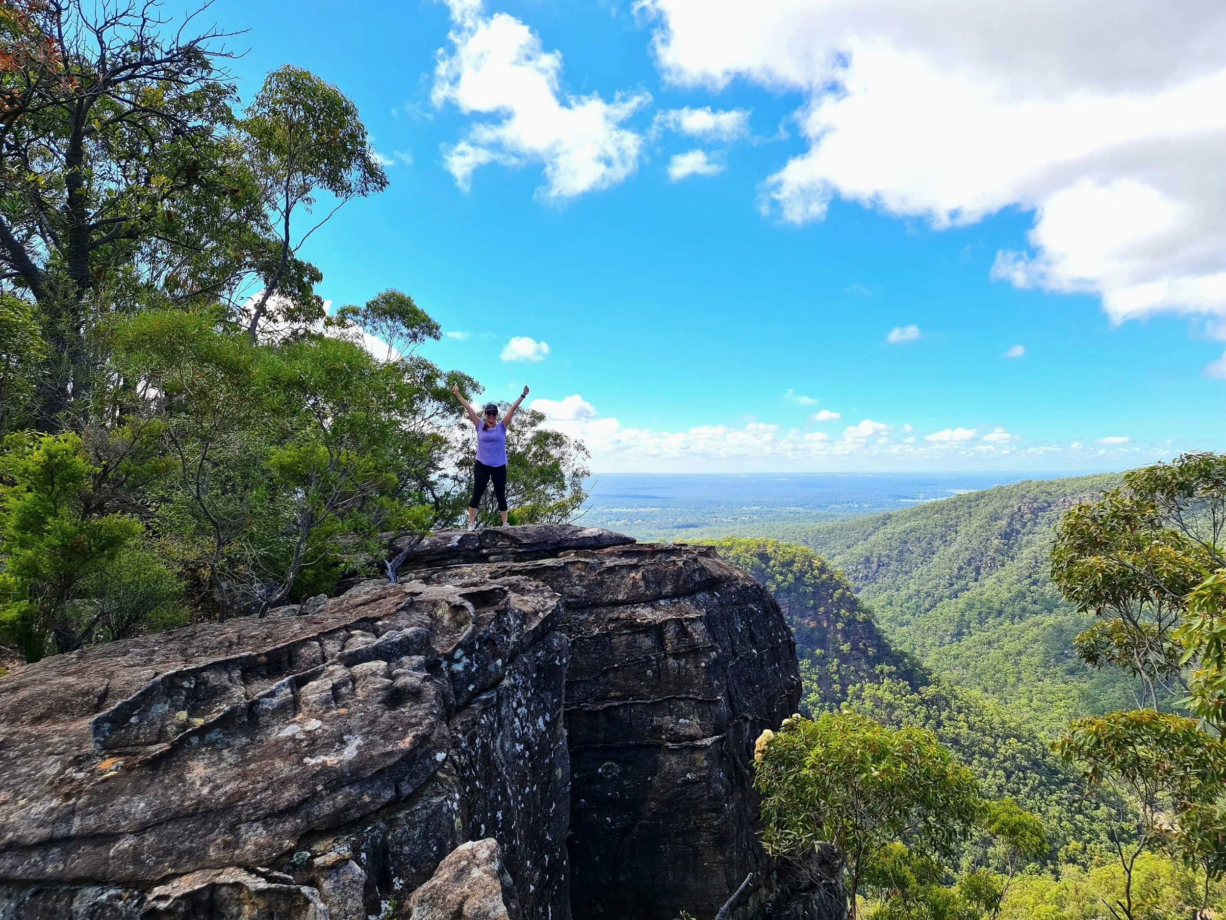 Guest enjoying a scenic bushwalk near Dido’s Place, standing on a rocky lookout above the Hawkesbury Valley surrounded by native forest and sweeping mountain views.