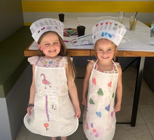 Two children wearing decorated aprons and chef hats during a school holiday activity at R.G. McGee's in the Hawkesbury NSW