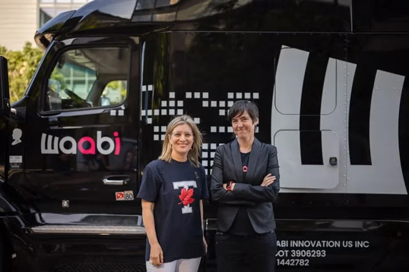 Two people stand in front of a black truck with “waabi” branding, posing side by side outdoors.