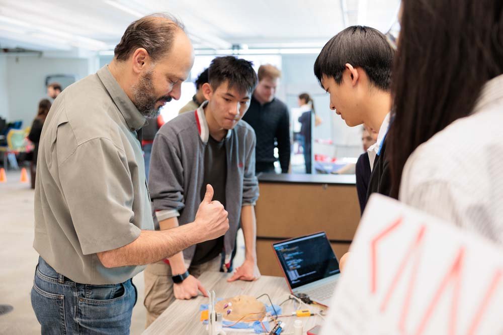 Professor and Chair Eyal de Lara engages with a project with students looking on.