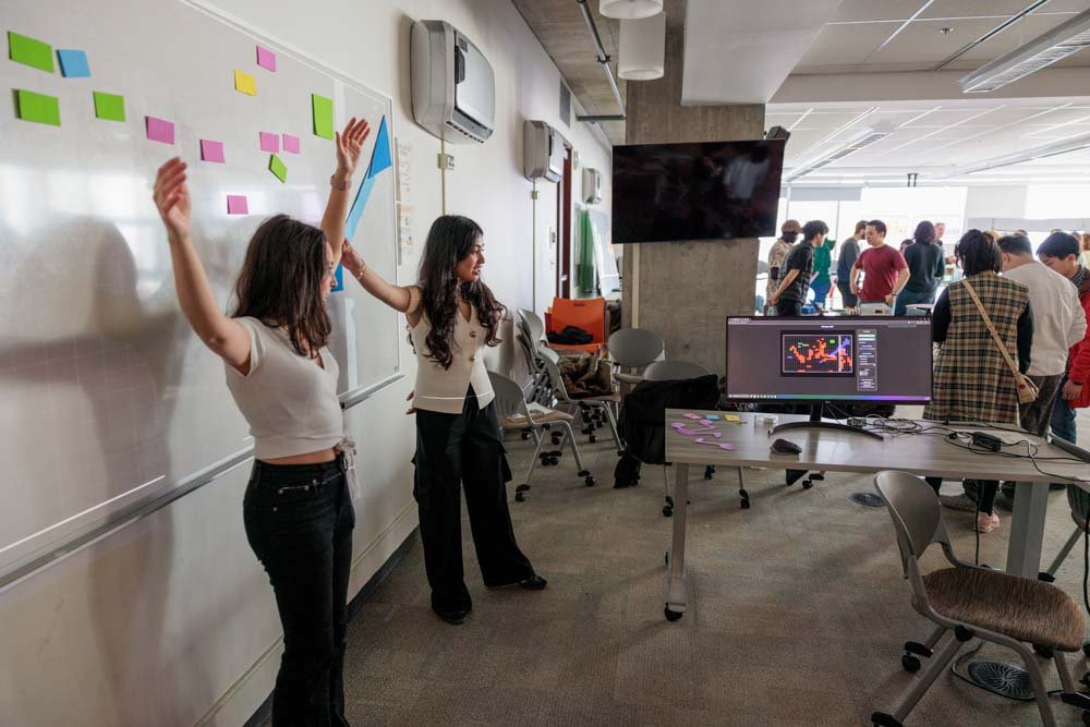 Students strike a pose in front of a whiteboard, looking at a computer screen that detects their movements