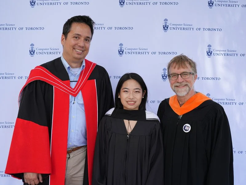  Three individuals in academic regalia standing in front of a 'Computer Science University of Toronto' backdrop. They wear gowns in red and black, black with white accents, and black with an orange hood, respectively. 
