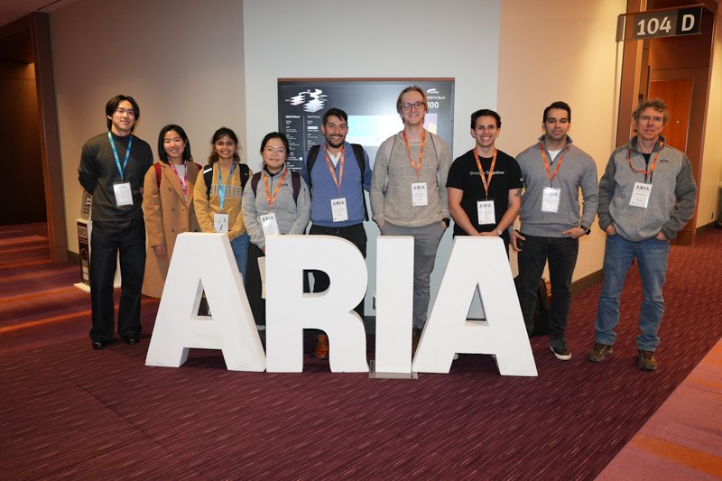  Group of people standing behind large white letters spelling “ARIA” in a hallway at the event venue. 