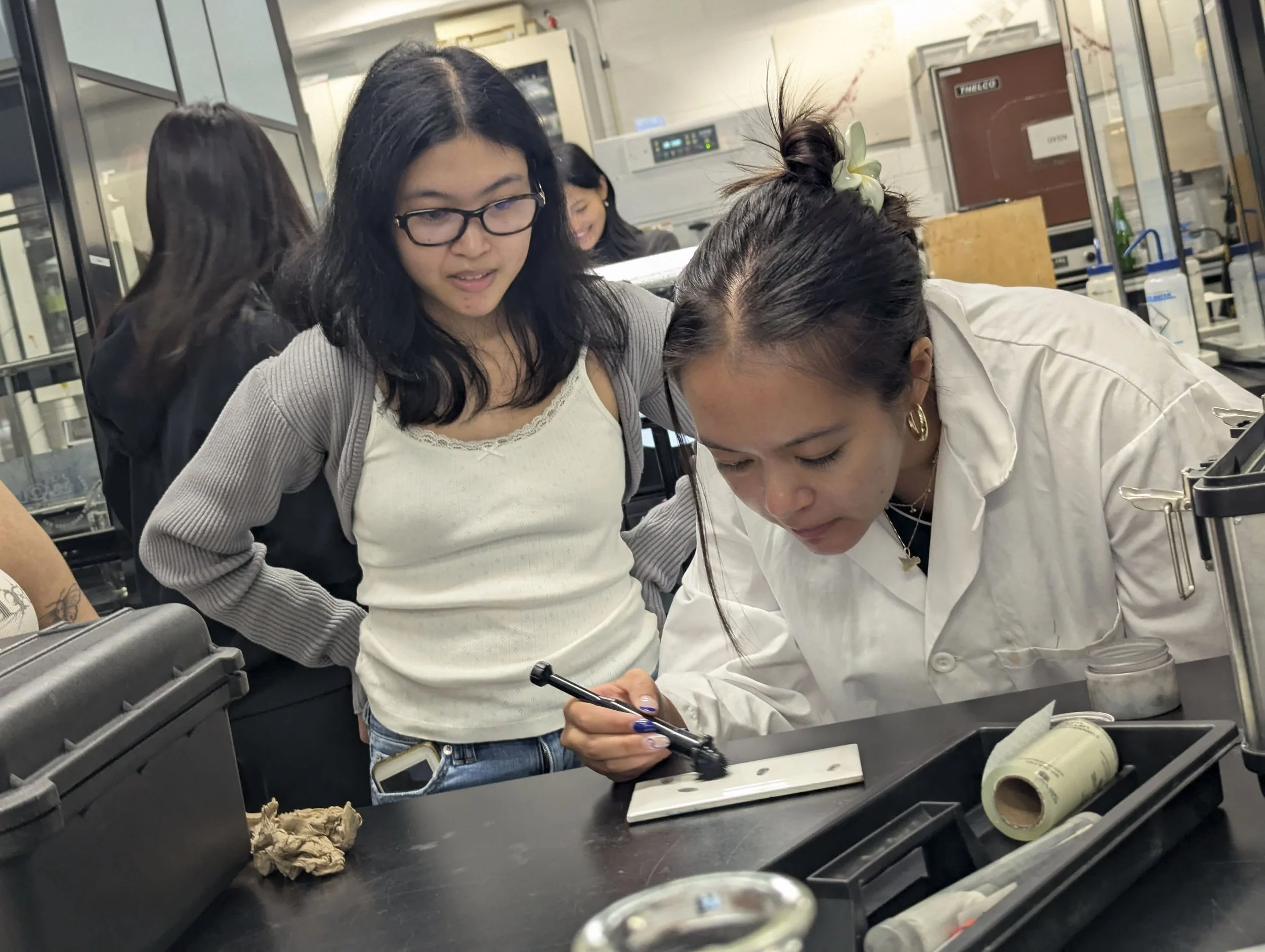 One student conducts fingerprint analysis while another student watches.