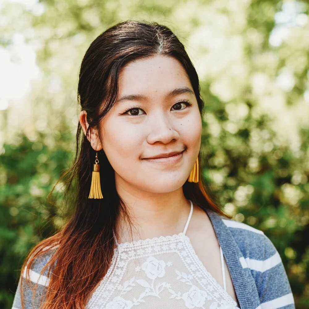 Blue (Georgianna) Lin smiles facing the camera. Green foliage is in the background.