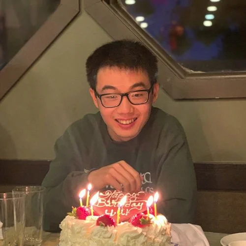 Yu Sun is smiling at a table with a birthday cake and candles in front.