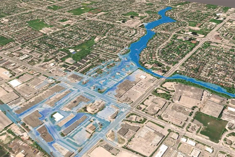 Oblique 3D aerial view of an urban area with blue overlay showing floodwater spreading from a winding river through residential streets, a major intersection, and commercial parking lots.