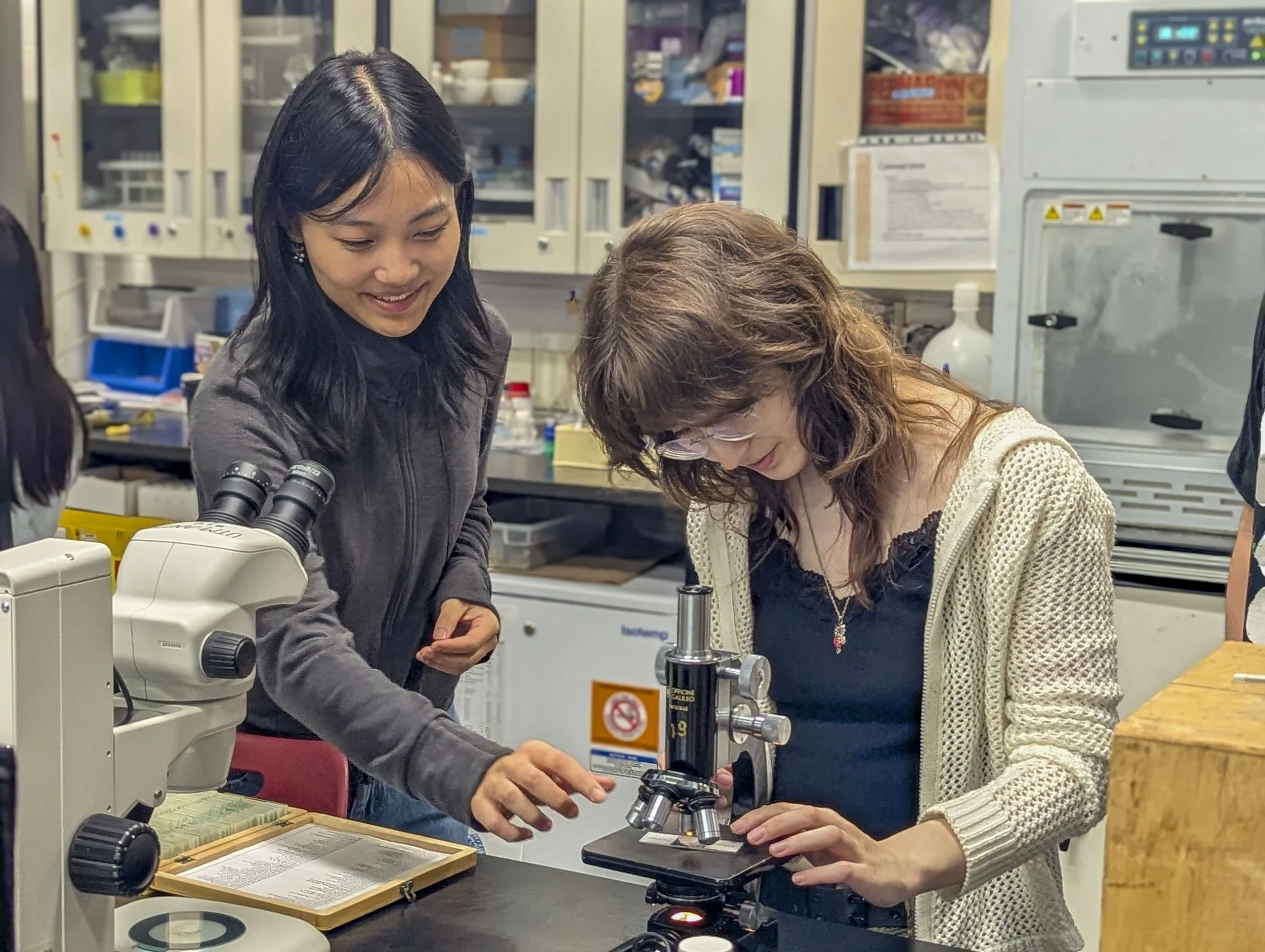 Two students examine specimens under a microscope.