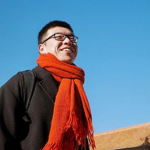 Weiyang "Frank" Wang is smiling looking off to the side. A blue sky is in the background.