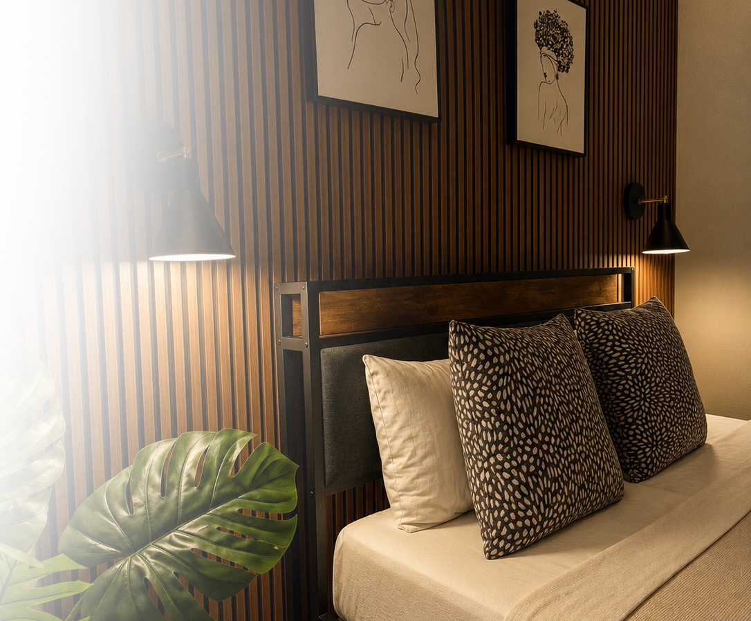 Modern bedroom with wooden slat wall, wall-mounted black lamps, framed line art portraits, a bed with white sheets, and patterned pillows, accented by a green tropical plant.