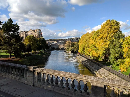 Pulteney Bridge and the horseshoe-shaped weir on the River Avon in Bath, England, on a bright day.