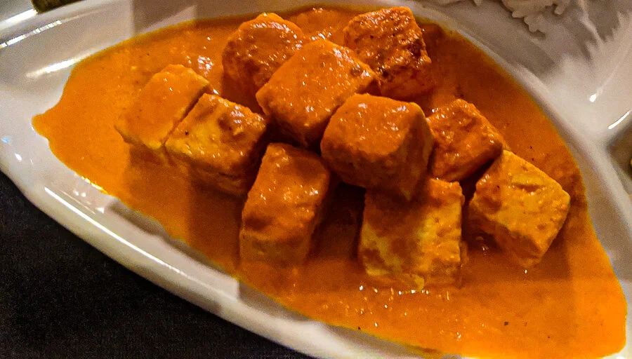 A close-up of Malai Paneer curry with soft cottage cheese cubes in a rich tomato and cream-based gravy.