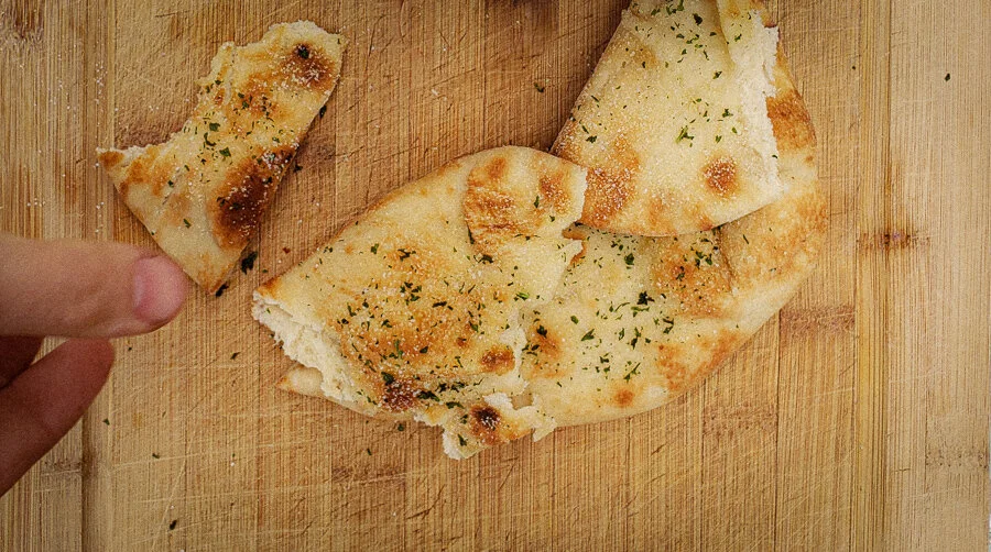 Freshly baked Garlic Naan bread with charred blisters and cilantro, prepared in a traditional clay tandoor oven.