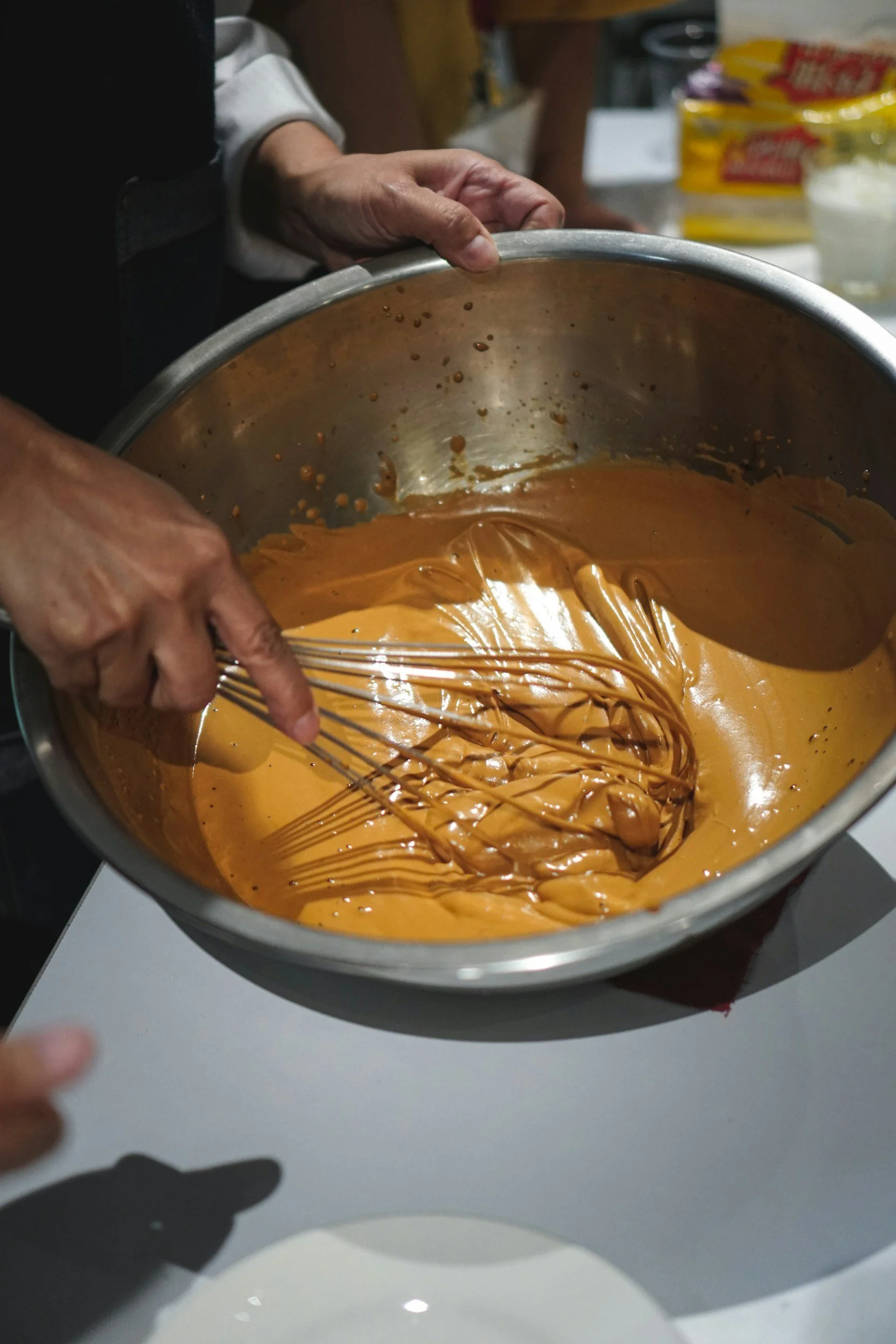 A close-up of a wire whisk stirring a smooth, creamy sauce in a metal pot.