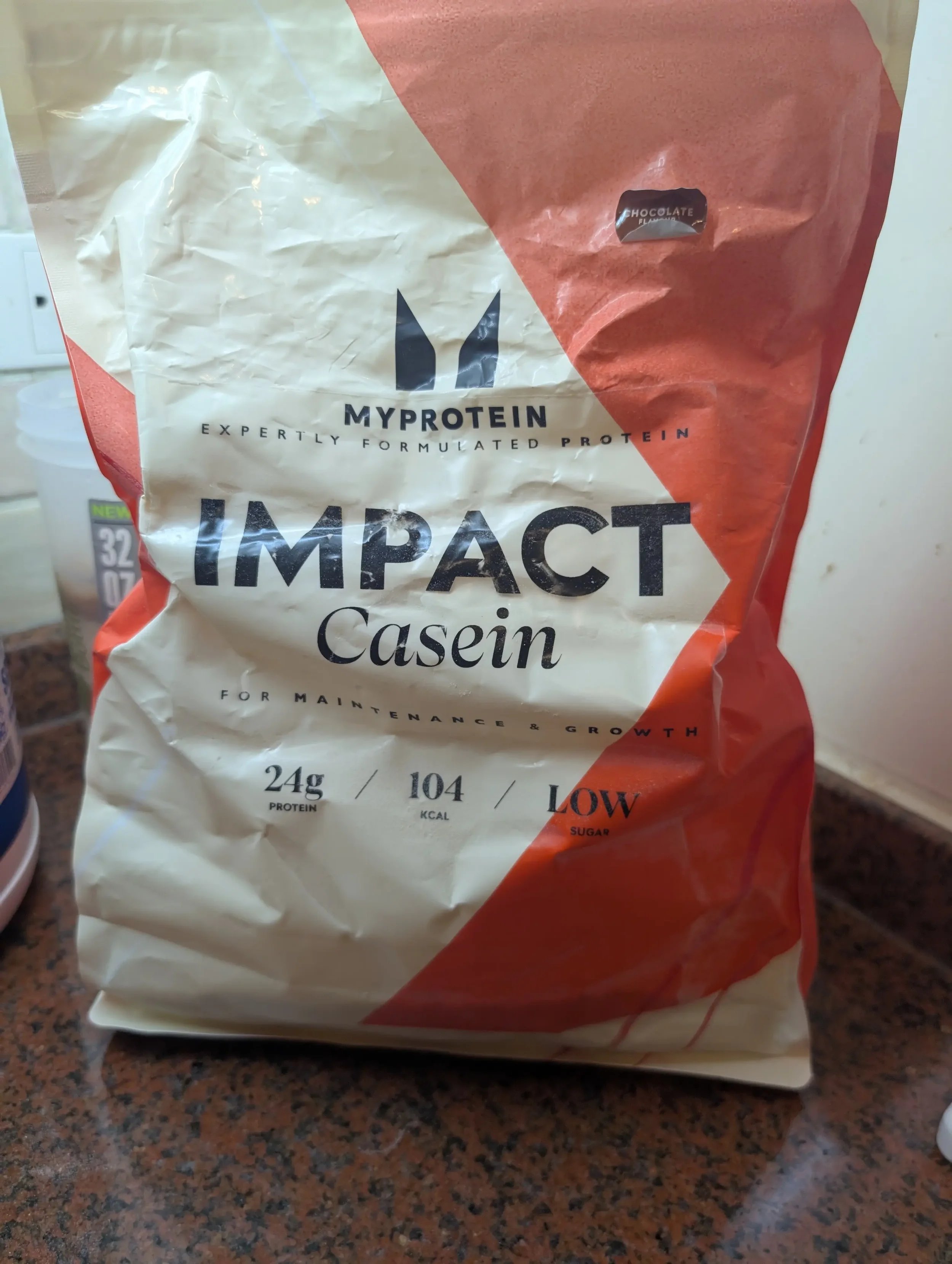 A bag of MyProtein Impact Casein protein powder in chocolate flavor sitting on a granite kitchen counter.