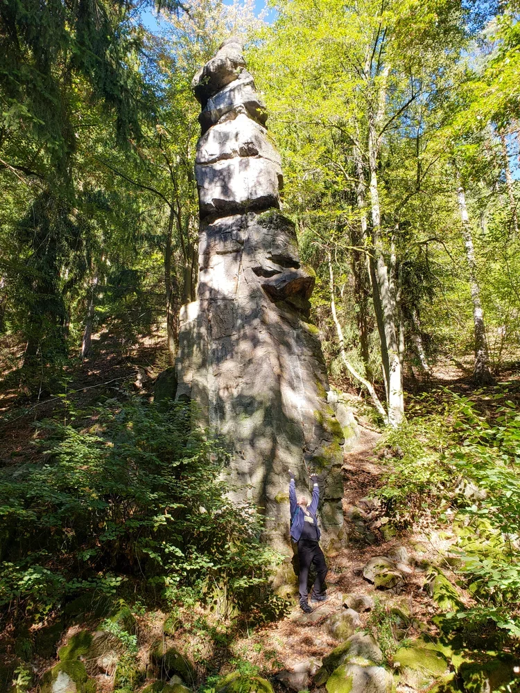 A tall granite rock spire surrounded by lush forest on a hiking trail in Slavkov Forest.