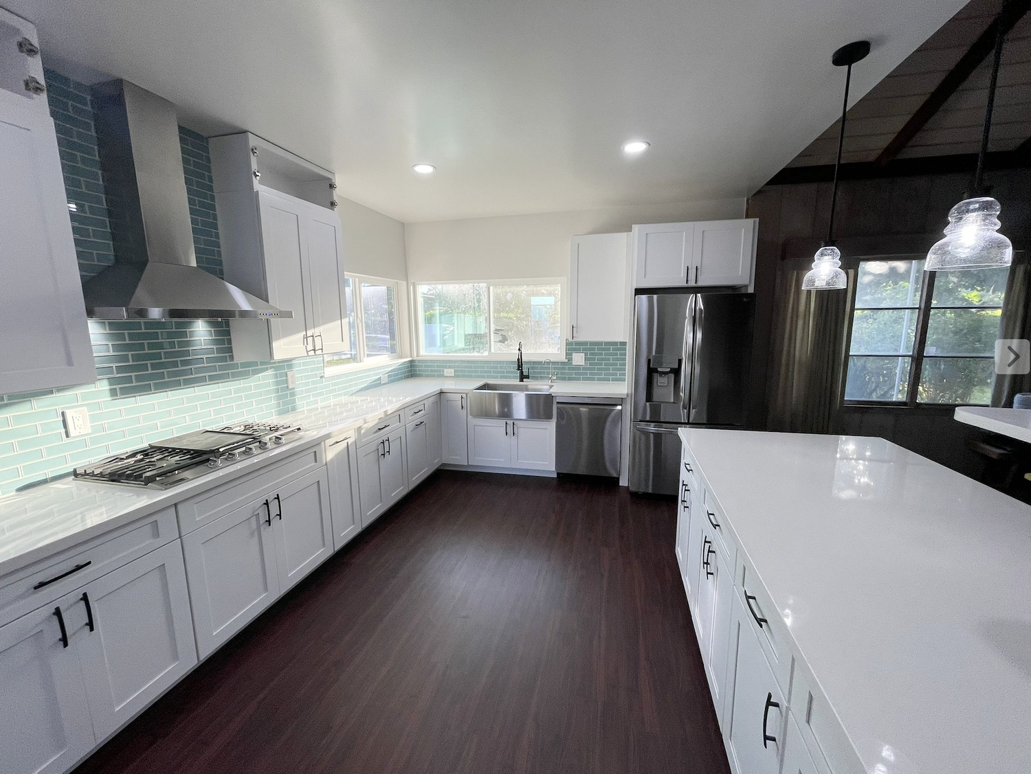 Modern kitchen with white cabinets, teal subway tile backsplash, stainless steel appliances, dark wood floor, and pendant lights.