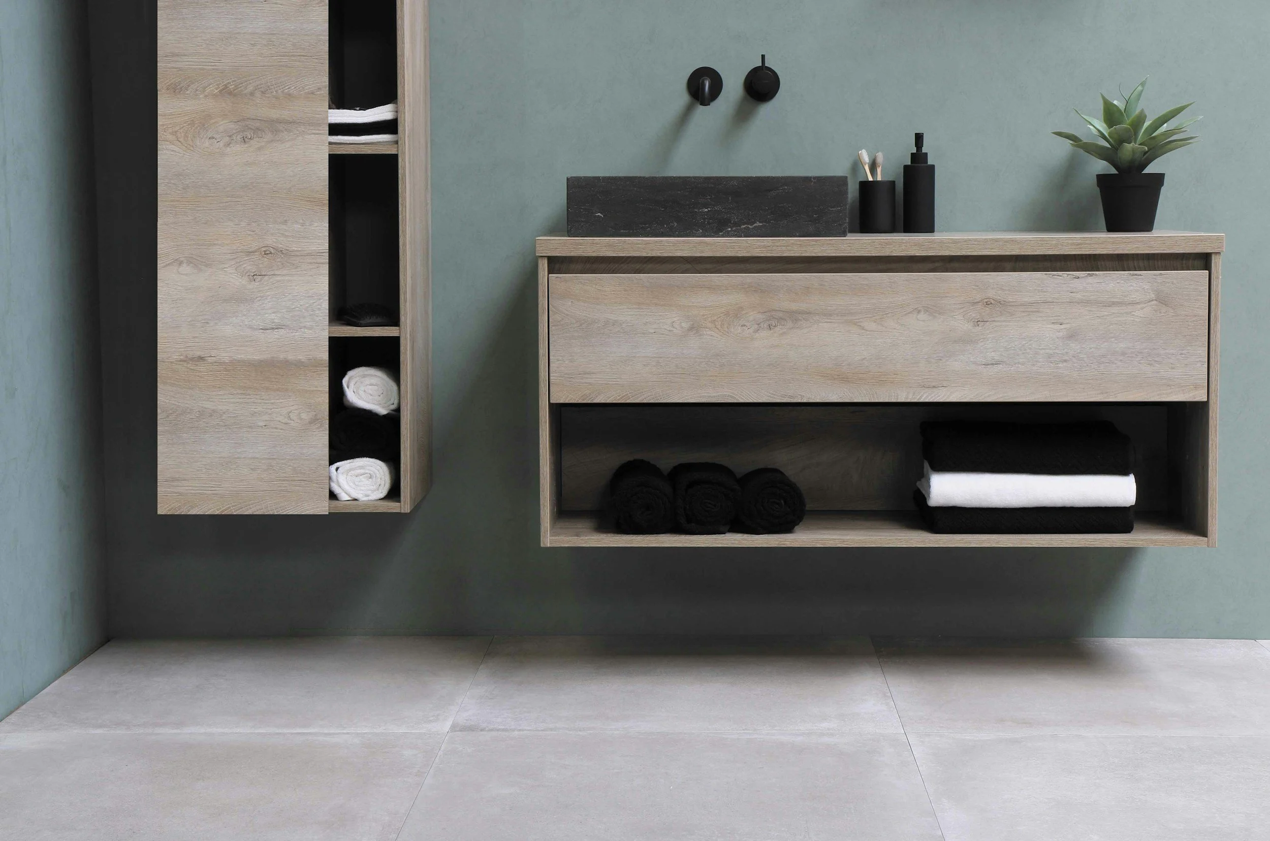 Modern bathroom vanity with a gray stone sink, black soap dispenser, toothbrush holder, and potted succulent plant, with drawers and open shelves containing rolled black and white towels.