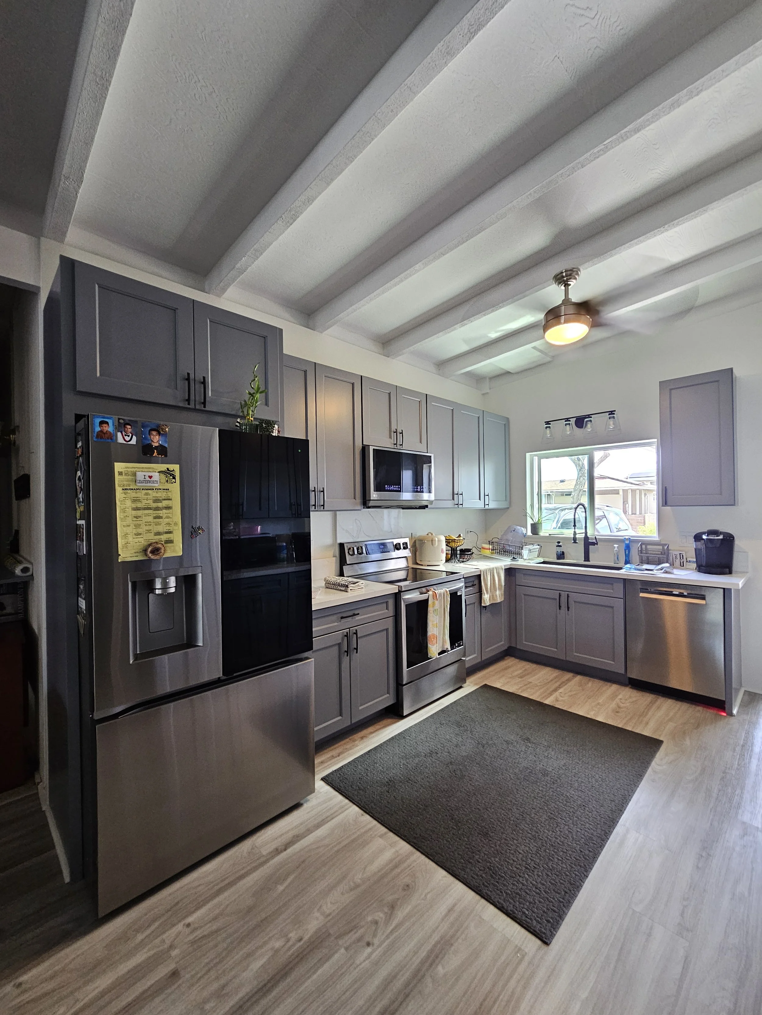 Modern kitchen with gray cabinets, stainless steel appliances, a black refrigerator, microwave, oven, and dishwasher, a window above the sink, and a ceiling fan.