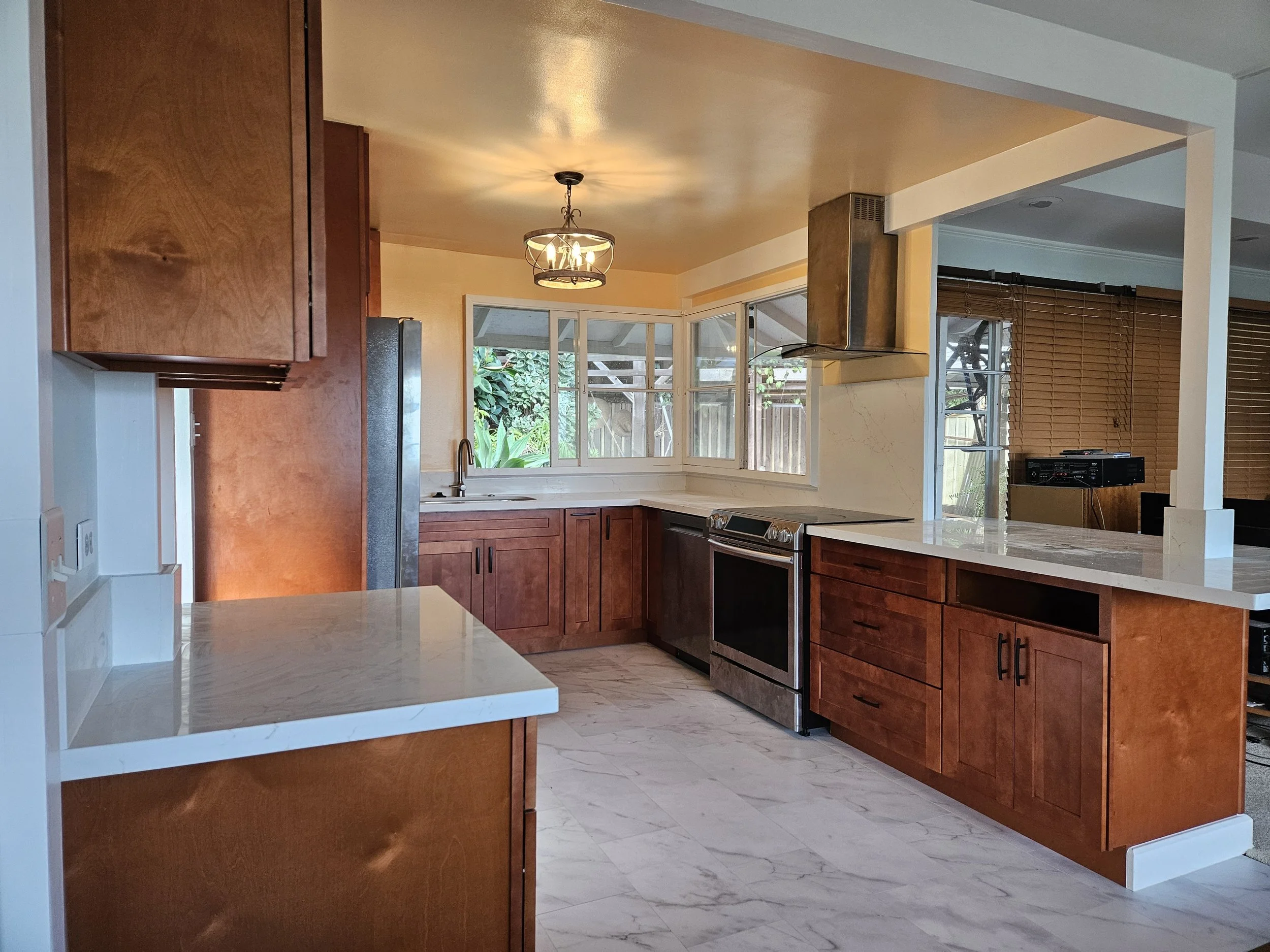Kitchen with wooden cabinets, marble countertops, stainless steel appliances, and a view of a backyard through windows.