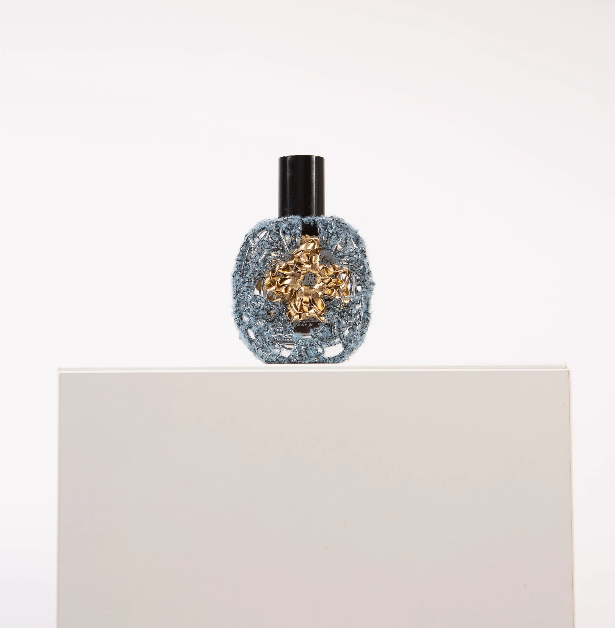 Golden perfume bottle wrapped in hand-crocheted textile sculpture by Sophie Inard Paris